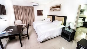 Habitación de hotel con dos camas, un escritorio, una silla, televisión y ventana con cortinas.