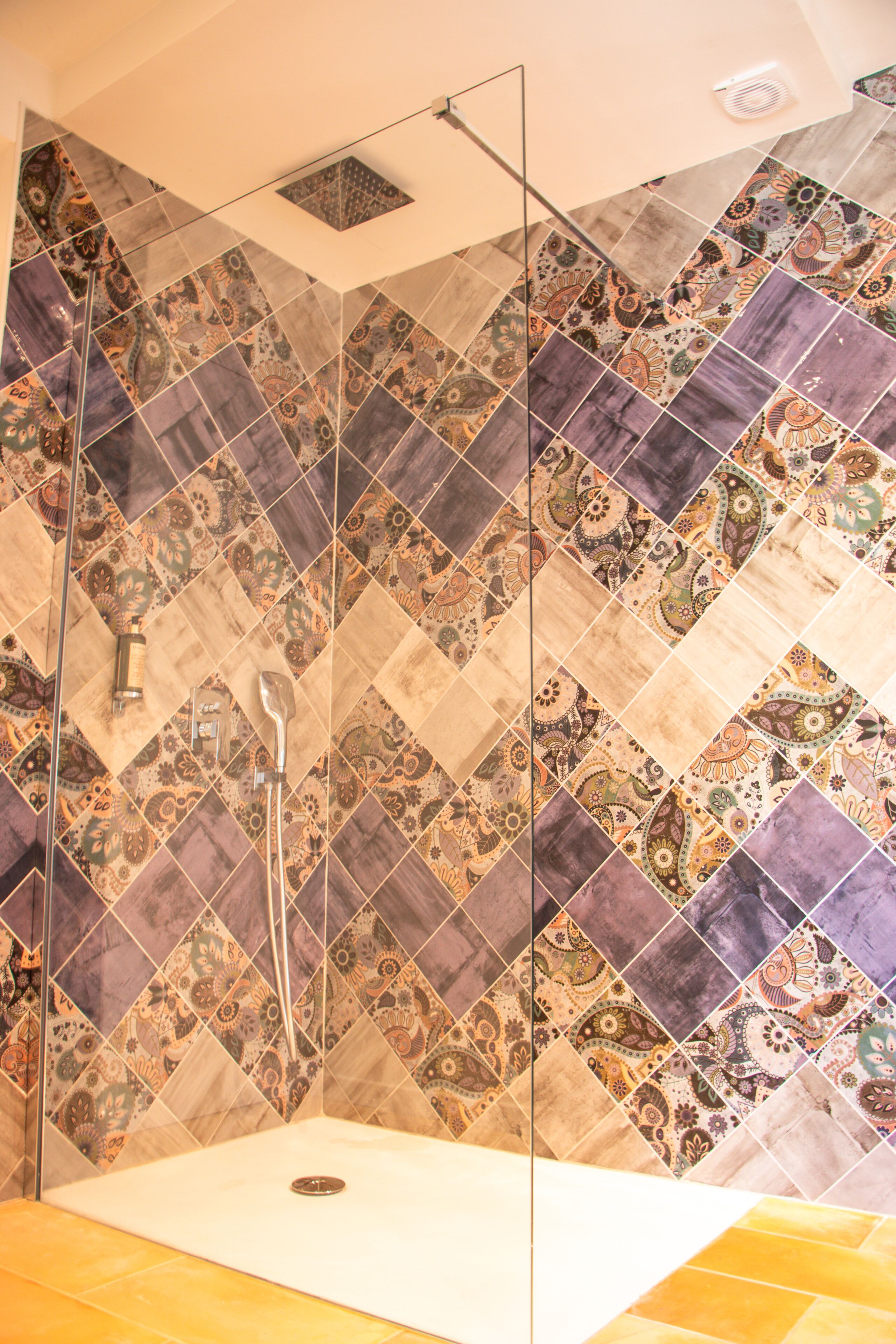 A shower area with a glass door and a tiled wall featuring a geometric pattern.