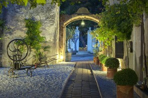A pathway leading to an arched entrance with a lantern above, surrounded by potted plants and a bicycle. - Château le Bouïs (Gruissan)