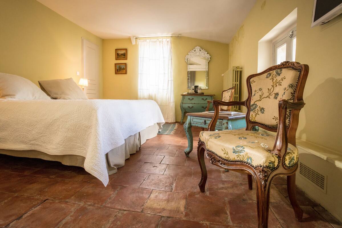 Un dormitorio con cama, una silla, cómoda y espejo.
