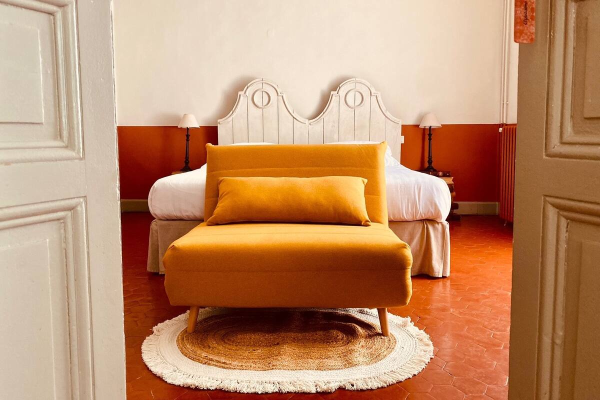 Un dormitorio con cama, mesita de noche, lámpara y alfombra redonda.