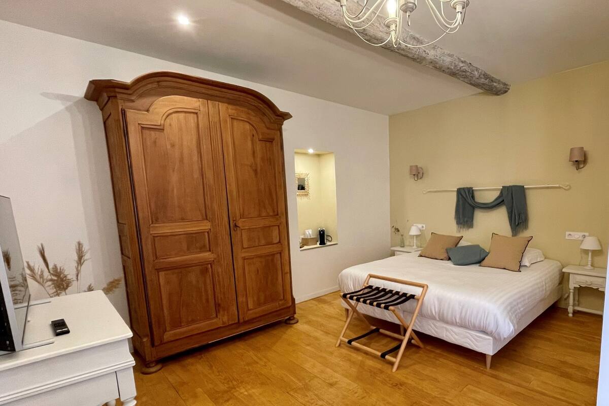 Un dormitorio con un armario de madera, una cama con almohadas, una mesita de noche con lámpara y una lámpara colgante.