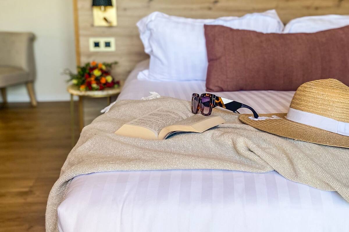 Una cama bien tendida con un edredón a rayas, un sombrero de paja y un par de gafas de sol.