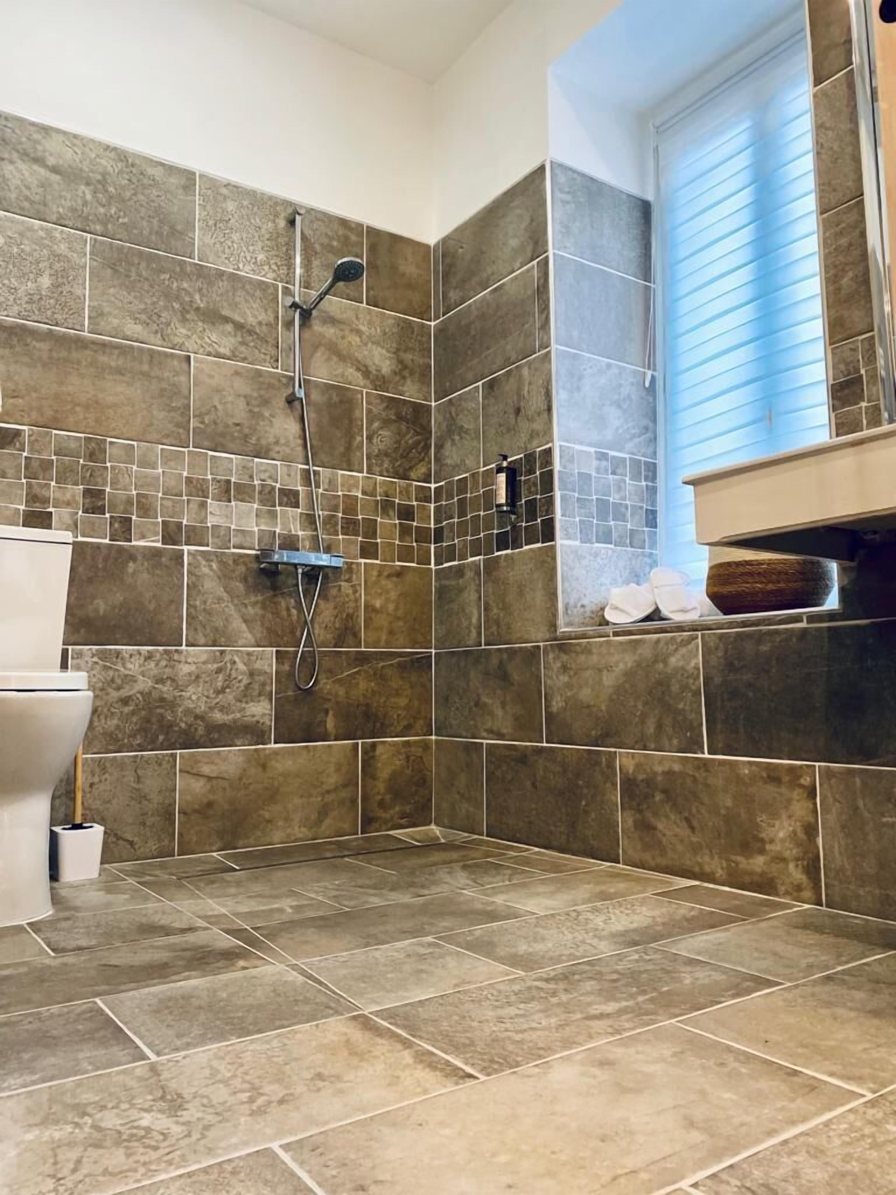A bathroom with a shower, tiled walls, and a window with blinds.