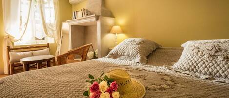 A cozy bedroom with a large bed, a small table, a chair, and a fireplace.