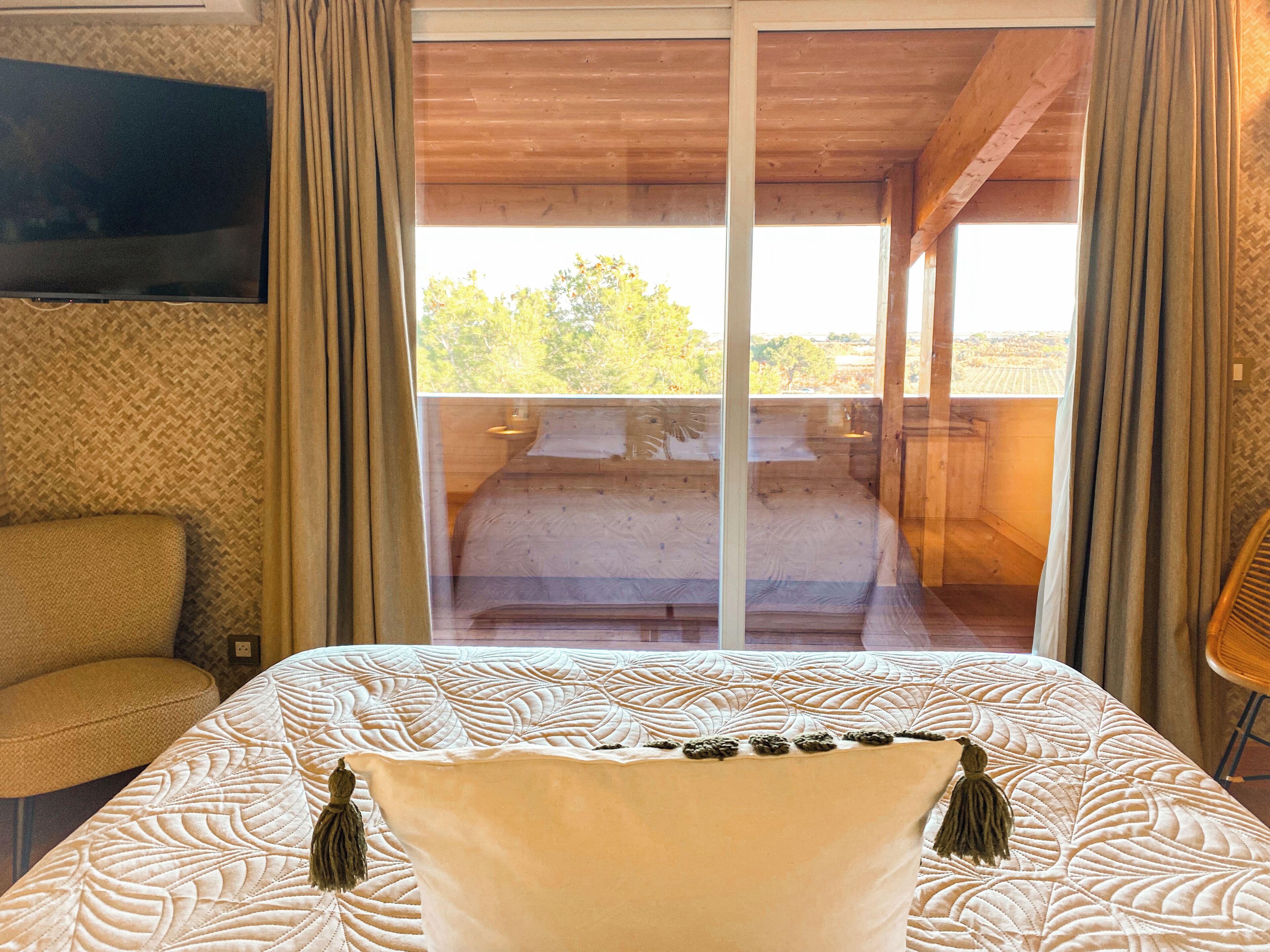 A bedroom with a large bed, a television on the wall, and a view of the outdoors through a sliding door.