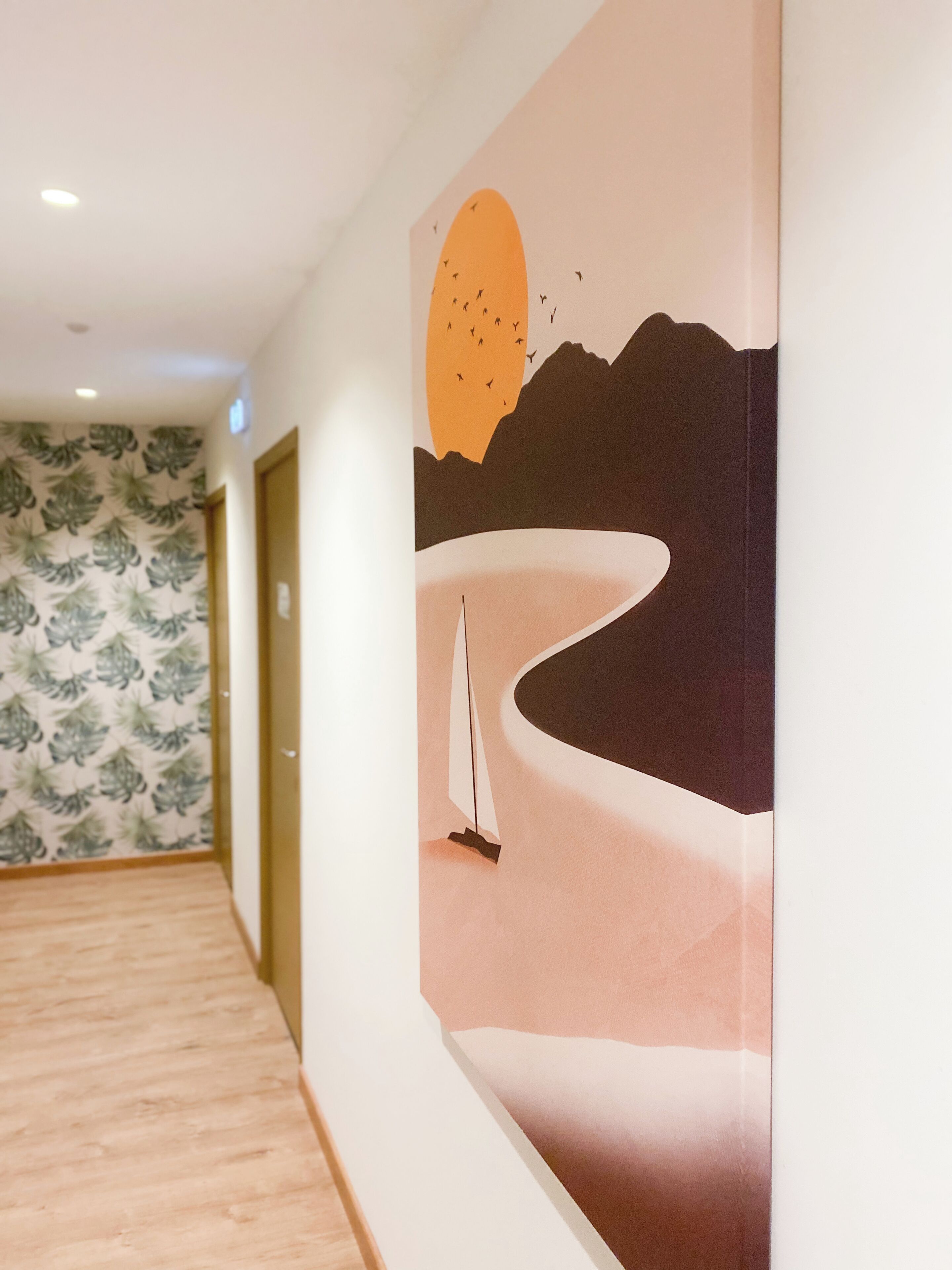 A hallway with a mural depicting a sailboat on a calm sea, a sunset, and mountains in the background.
