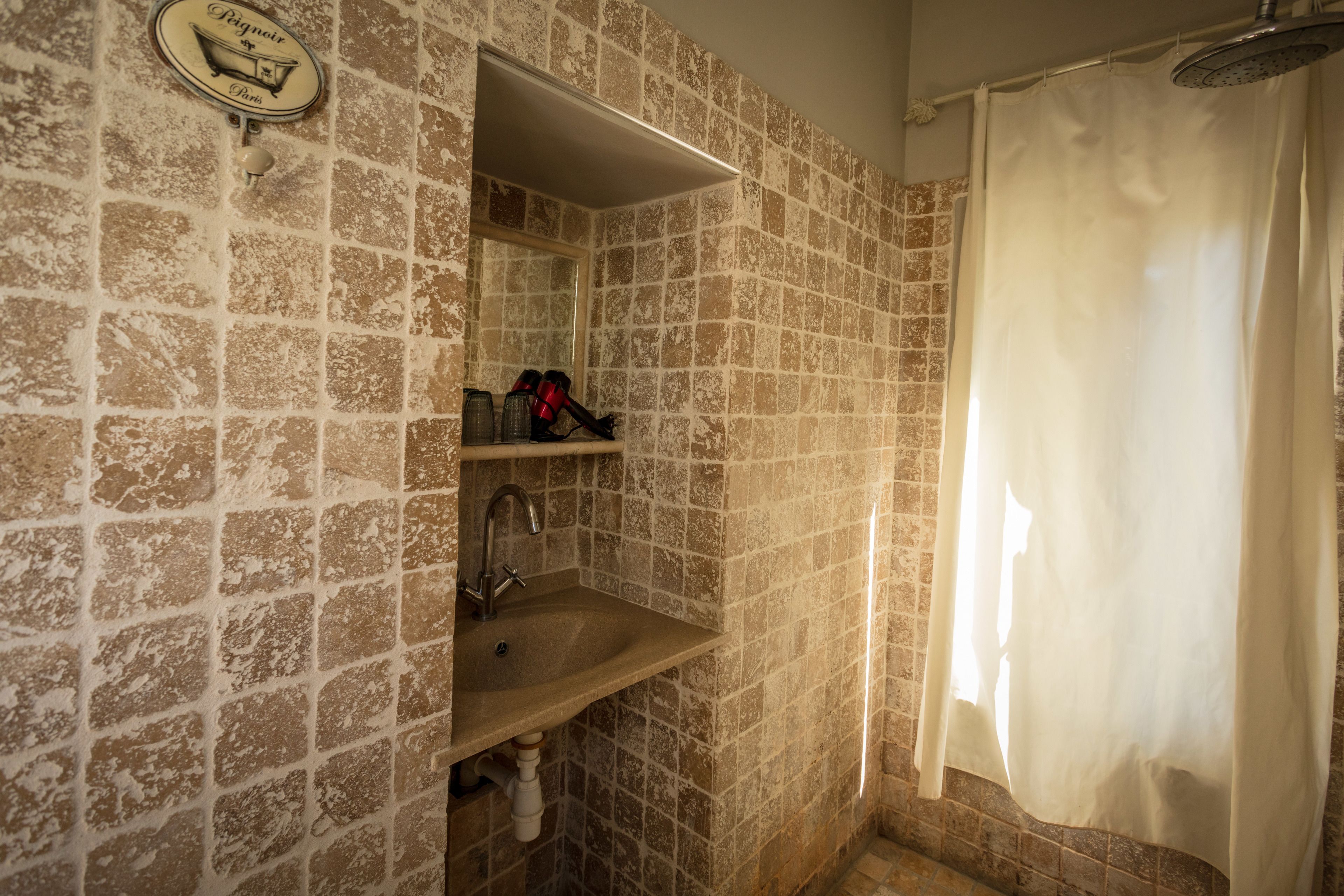 Un baño con pared de azulejos, un lavabo, un espejo y una cortina de ducha.
