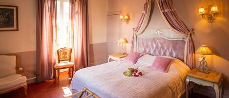 A bedroom with a large bed, a chair, a nightstand, and a lamp.
