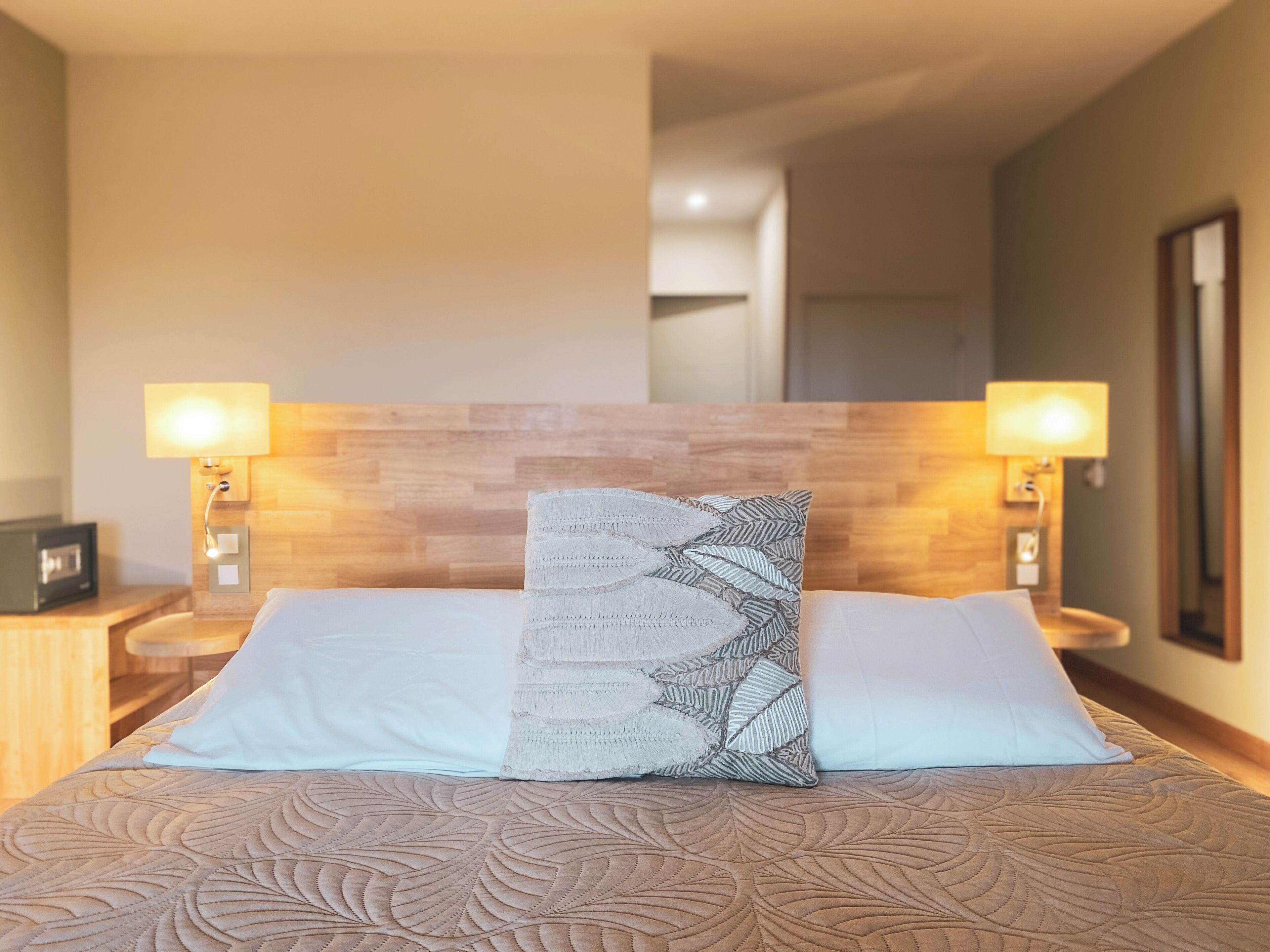 Habitación de hotel con una cama, dos lámparas de noche, una mesita de noche y un cabecero de madera.