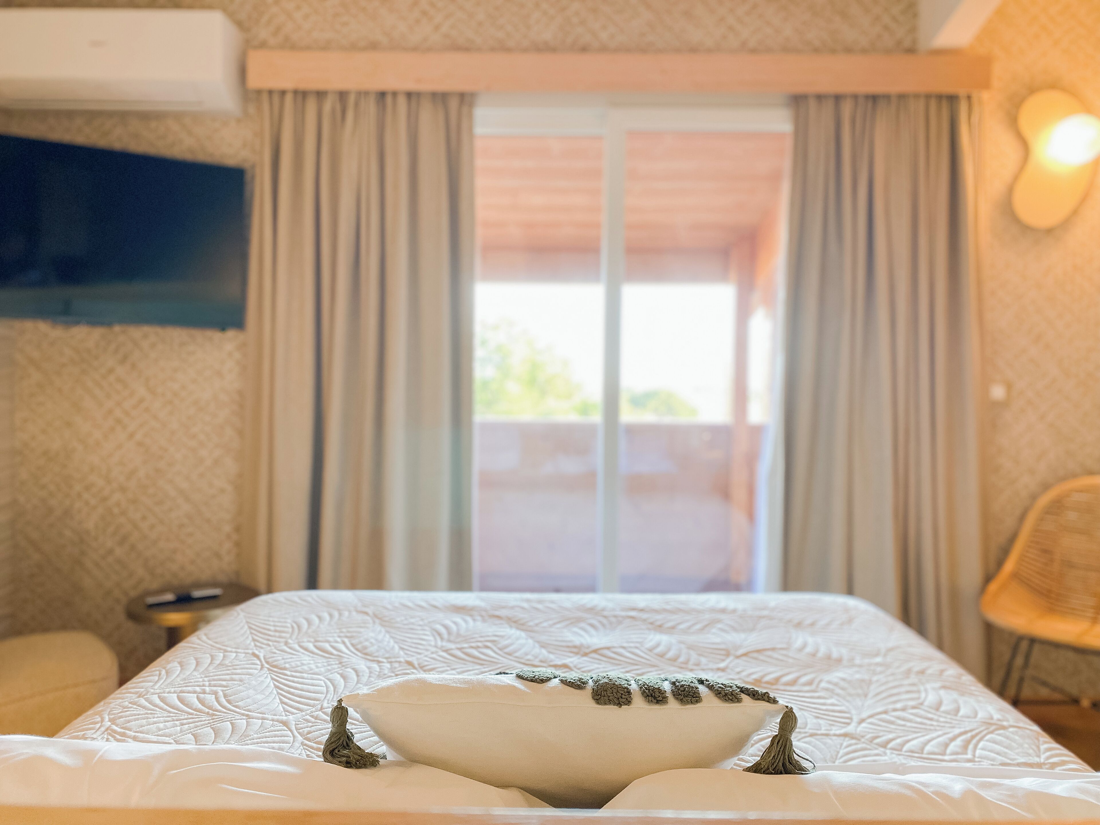Une chambre d’hôtel avec un lit, des rideaux, un téléviseur fixé au mur et une vue par la fenêtre.