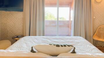 Une chambre d’hôtel avec un lit, des rideaux, un téléviseur fixé au mur et une vue par la fenêtre.