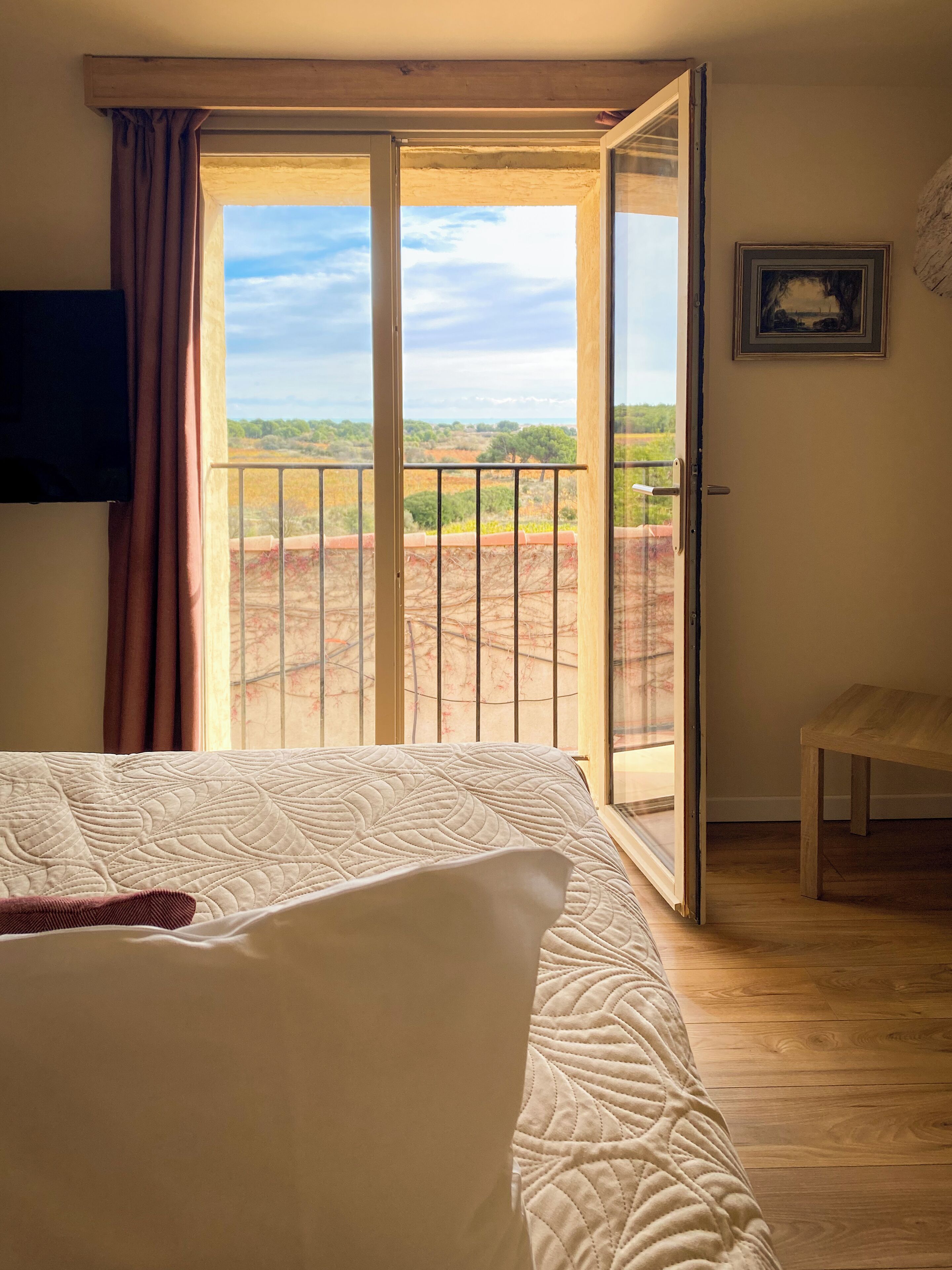 A bedroom with a large bed, a sliding glass door leading to a balcony, and a wooden floor.