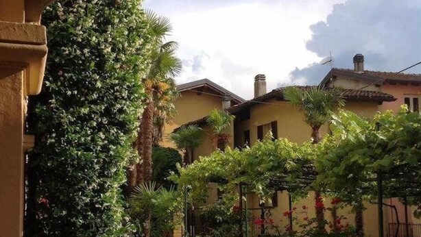 Une cour intérieure avec un chemin menant à un bâtiment à la façade jaune et à une zone abritée dotée d’une pergola.