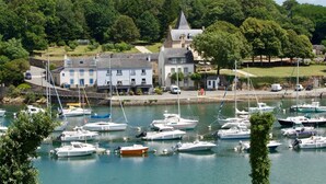 Un port de plaisance où sont amarrés de nombreux bateaux, un bâtiment doté d’une tour et, au loin, une colline verdoyante.