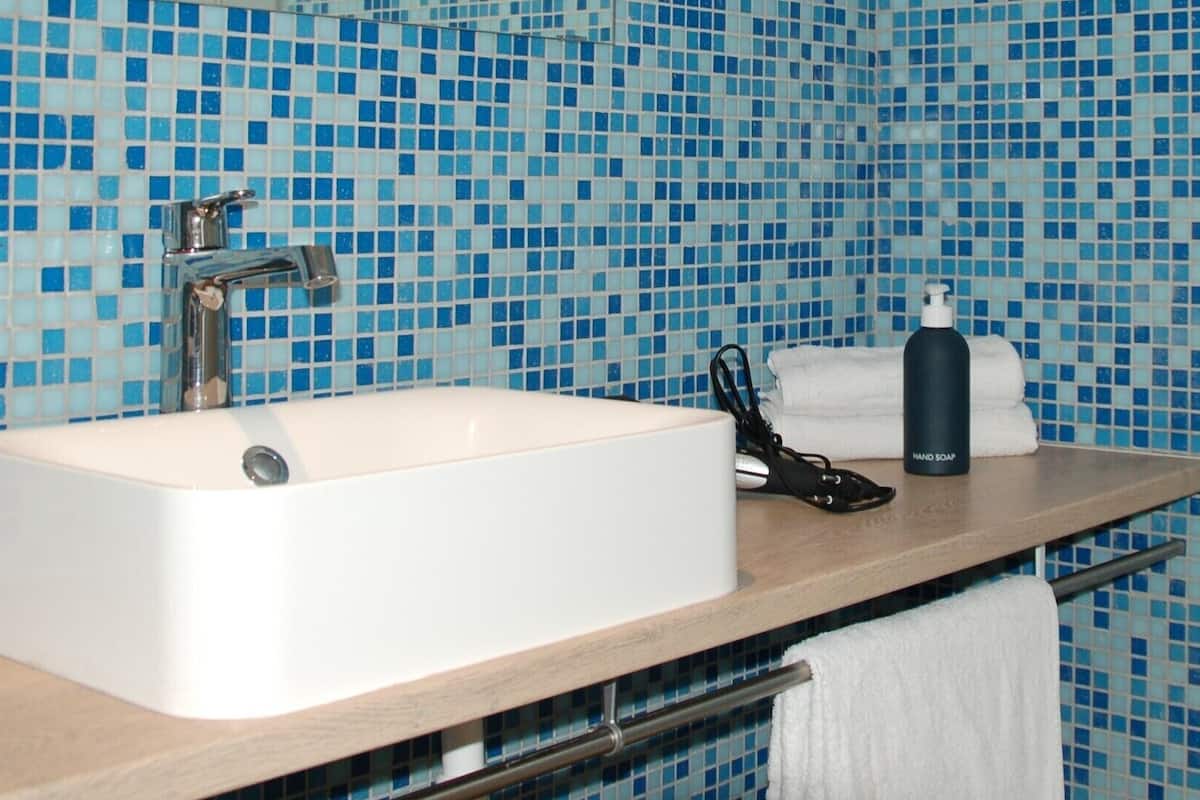 Une salle de bain avec un lavabo blanc, un miroir et un mur recouvert de mosaïques bleues.