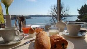 Une table de petit-déjeuner avec des croissants, du jus d’orange et des tasses de café, donnant sur un lac.