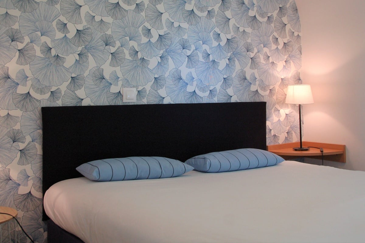 Une chambre d’hôtel avec un grand lit, deux lampes de chevet et un papier peint à motifs floraux.