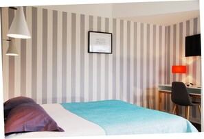 Une chambre d’hôtel avec un lit, un bureau et une chaise. Un mur est décoré de rayures et un tableau encadré est accroché au mur.
