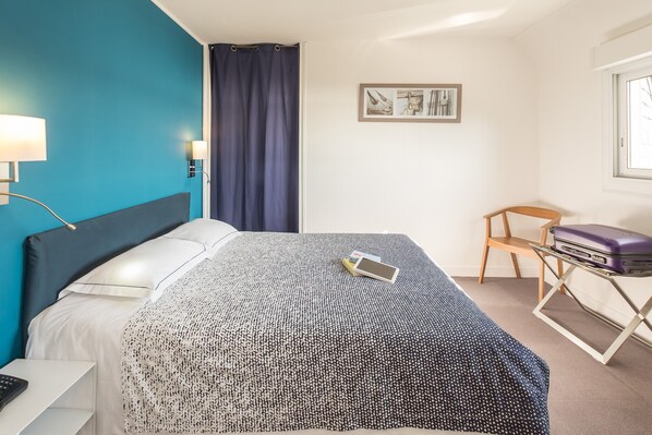 Une chambre d’hôtel avec un lit, un bureau, une chaise, une fenêtre et un rideau.