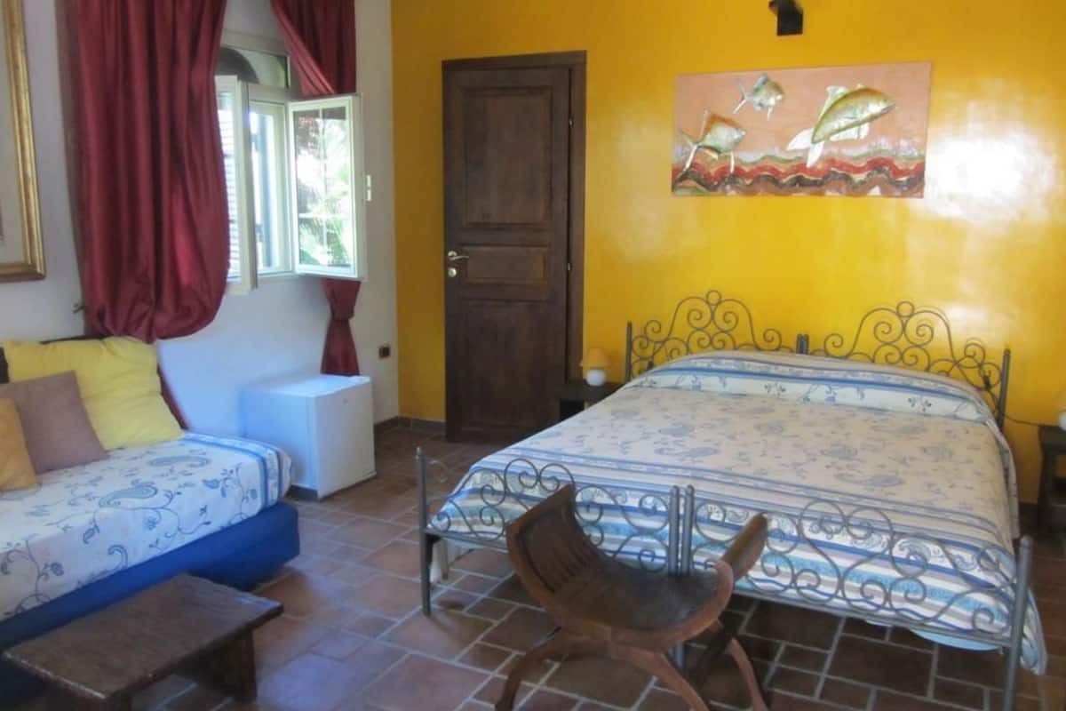 A bedroom with a bed, a chair, a sofa, and a window with curtains.
