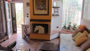 Una sala de estar acogedora con chimenea, un sofá con cojines estampados y vistas a través de un ventanal grande.
