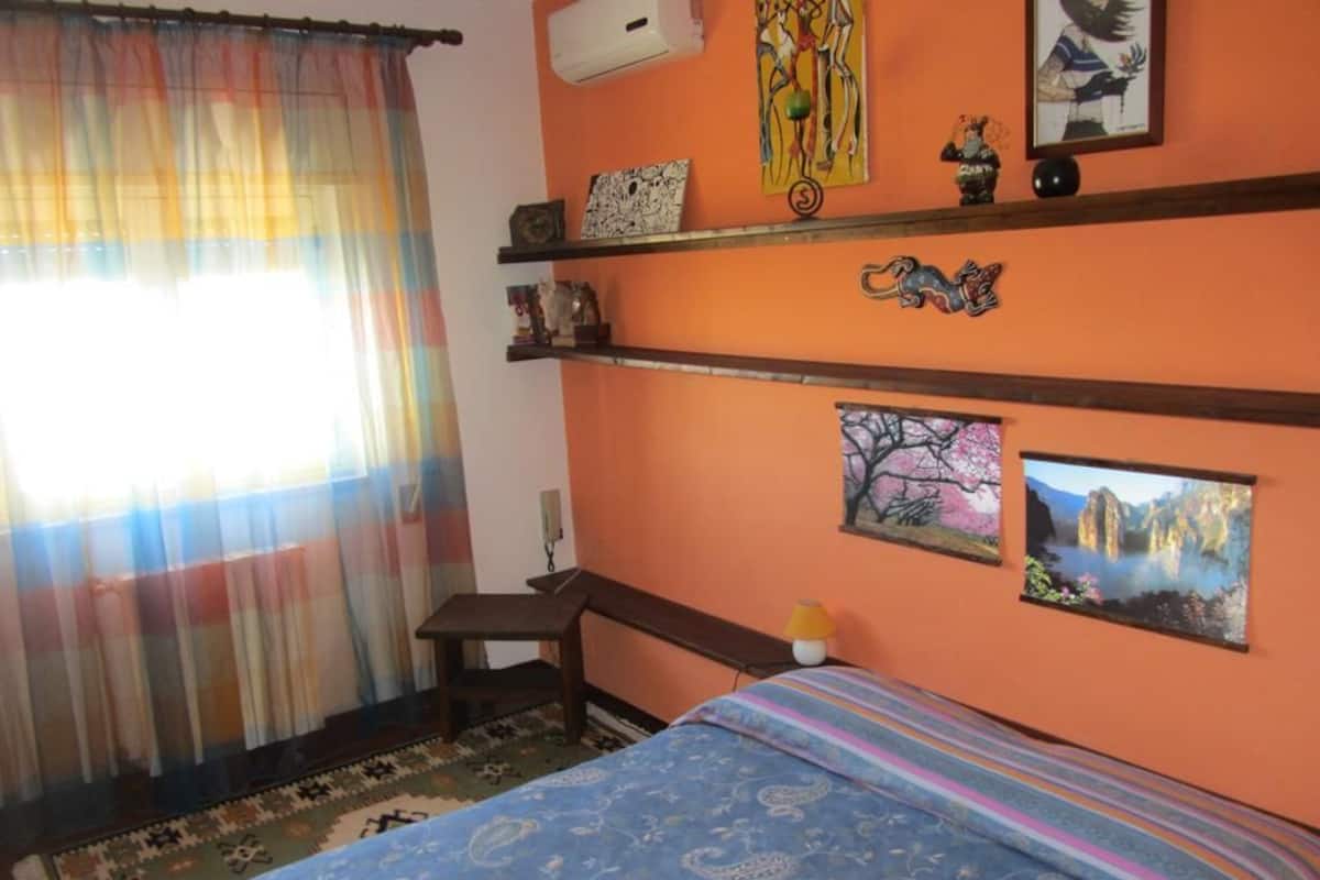 A bedroom with a bed, a desk, and two shelves with decorative items.