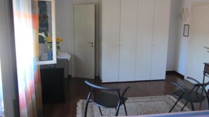 Una habitación con cama, dos sillas, un armario y una pequeña mesa con un florero.
