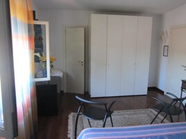Una habitación con cama, dos sillas, un armario y una pequeña mesa con un florero.
