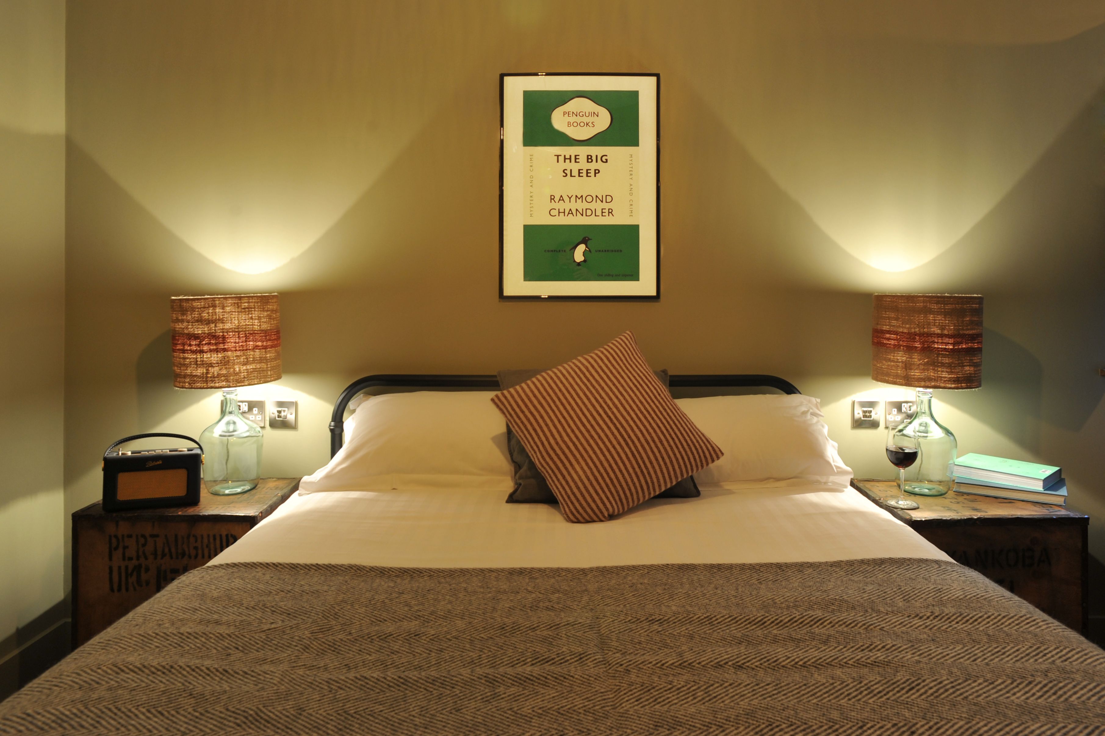 A neatly made bed with a pillow, two bedside lamps, a framed book on the wall, and a bottle on the nightstand.