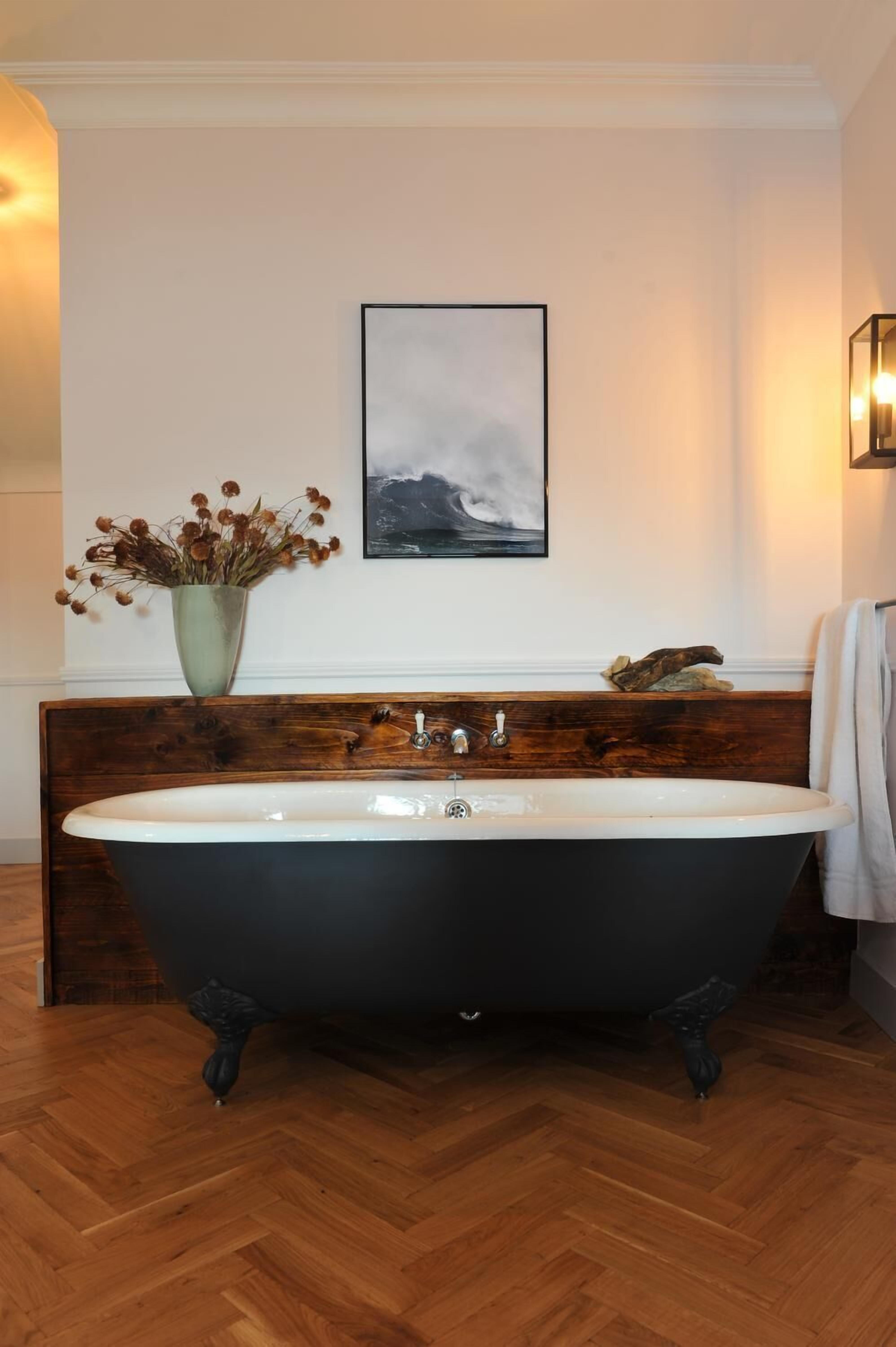 Un baño con una bañera independiente, un tocador de madera, un jarrón con flores secas y un cuadro en la pared.