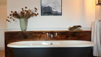 Un baño con una bañera independiente, un tocador de madera, un jarrón con flores secas y un cuadro en la pared.