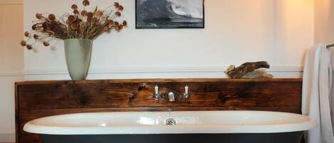 Un baño con una bañera independiente, un tocador de madera, un jarrón con flores secas y un cuadro en la pared.