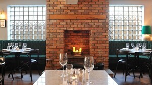 Un restaurante con paredes de ladrillo, chimenea, asientos tapizados en verde y mesas dispuestas para comer.