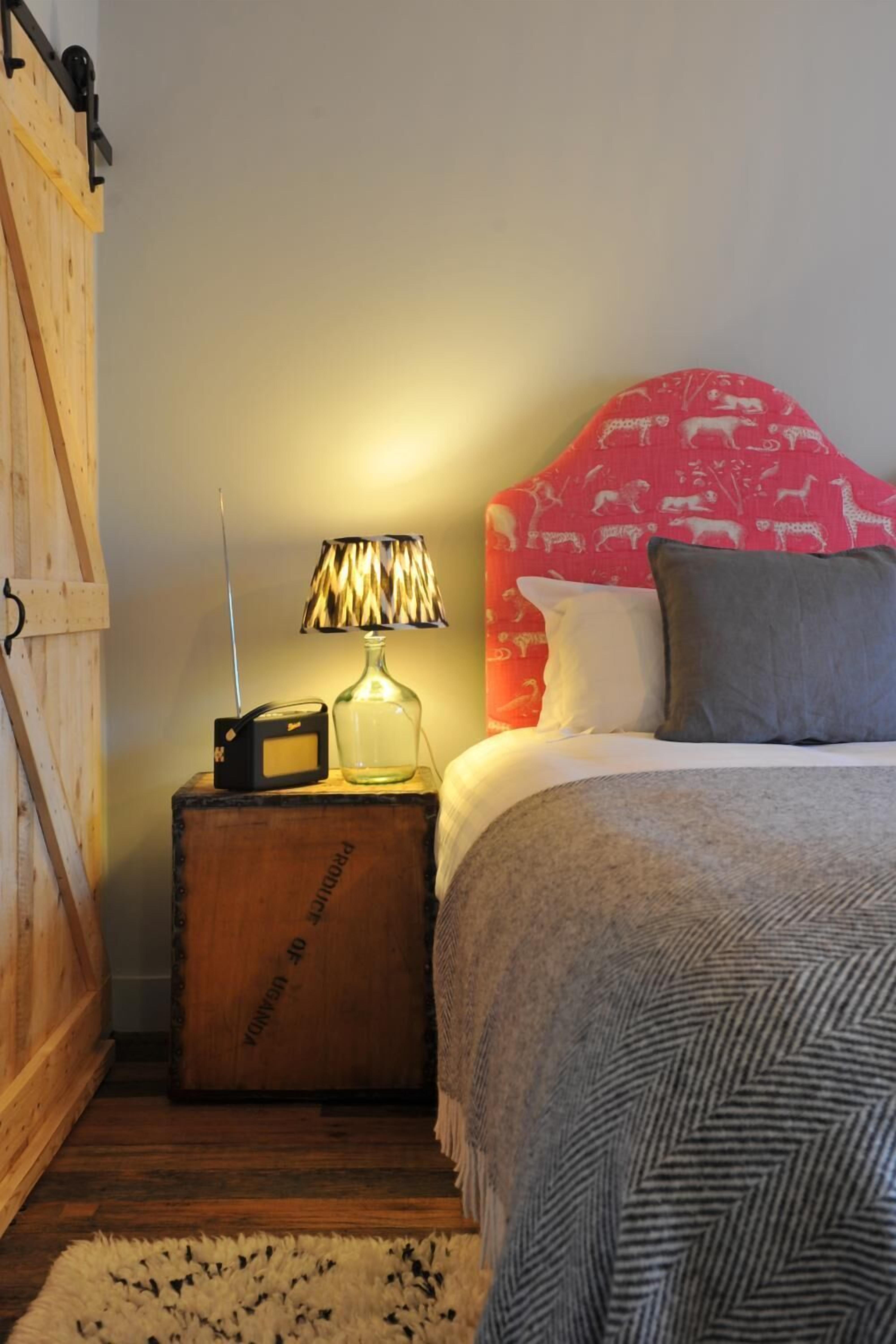 Una camera da letto con una testiera in legno, una radio su un ripiano di legno, una lampada e una coperta decorata.