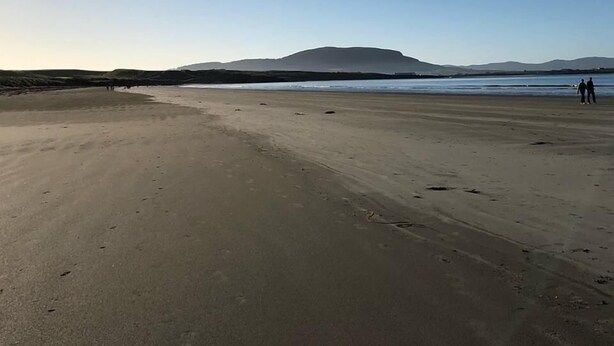 Una playa amplia y arenosa con cielo despejado y montañas a lo lejos.