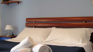 A neatly made bed with white linens and rolled towels, a wooden headboard, and a bedside table with a lamp. - Sea View Apartment (Ragusa)