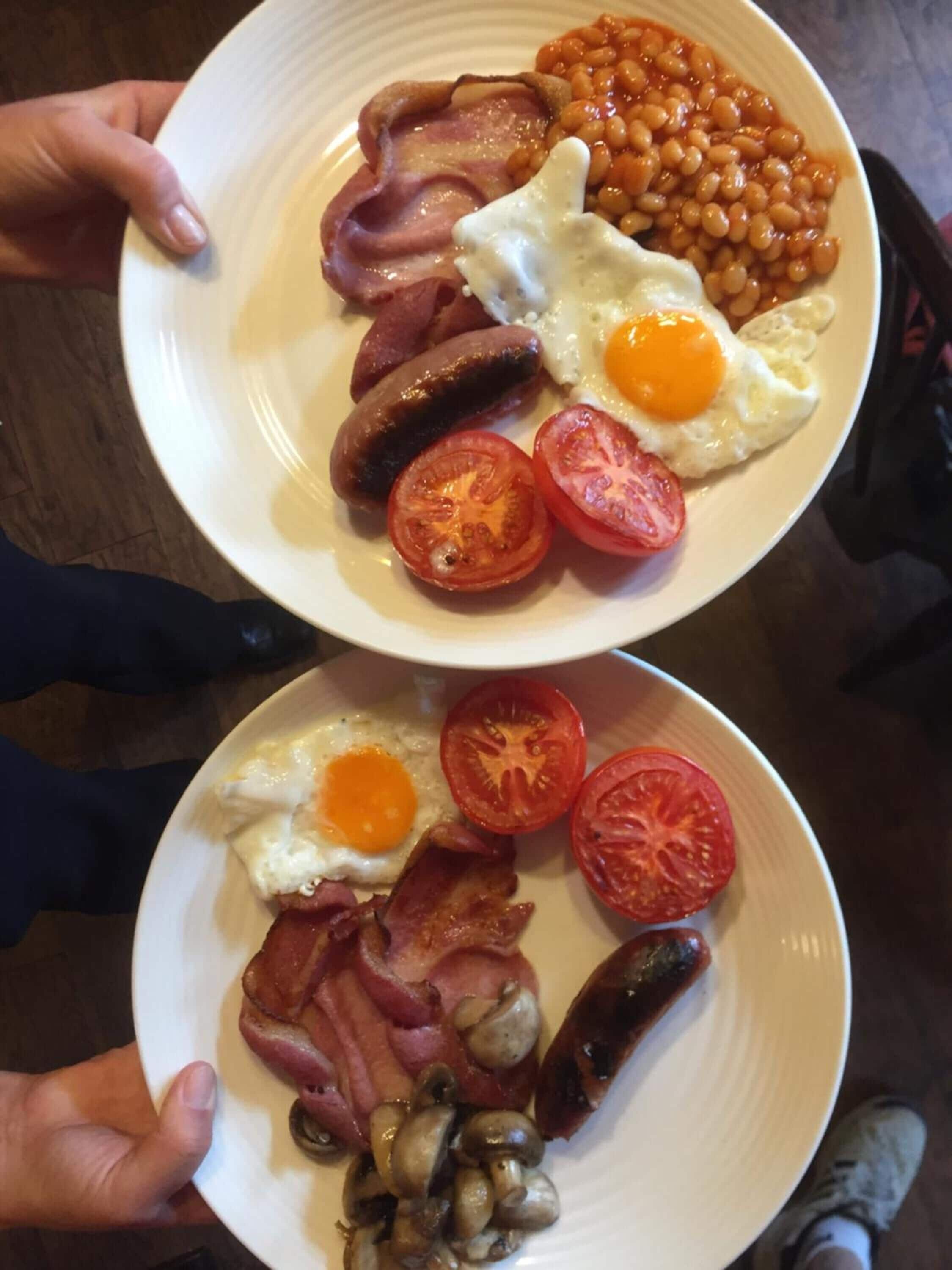 Due piatti di cibo per la colazione con uova, salsicce, pomodori e fagioli.