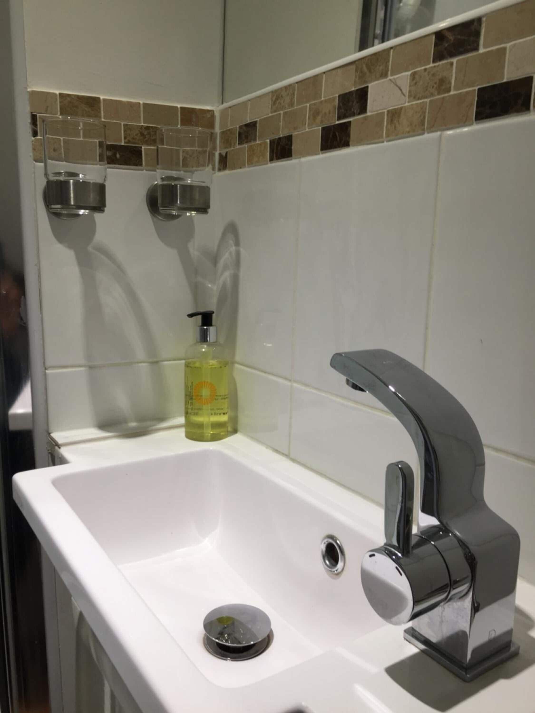 A bathroom with a white sink, chrome faucet, and a bottle of hand soap.