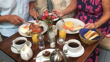Una mesa de comedor con alimentos para el desayuno, una cafetera y un florero con flores.