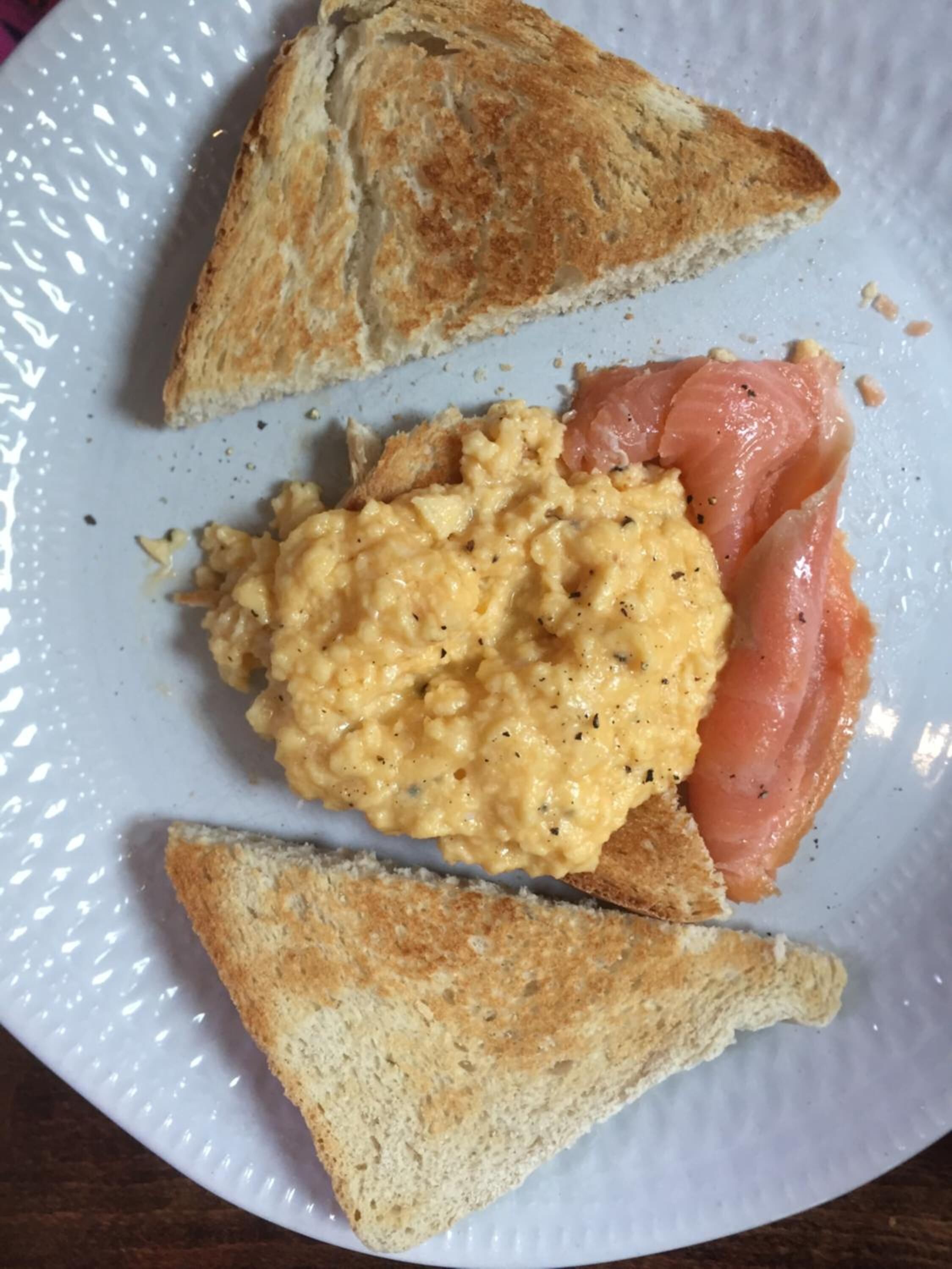 A plate with scrambled eggs, smoked salmon, and two slices of toast.