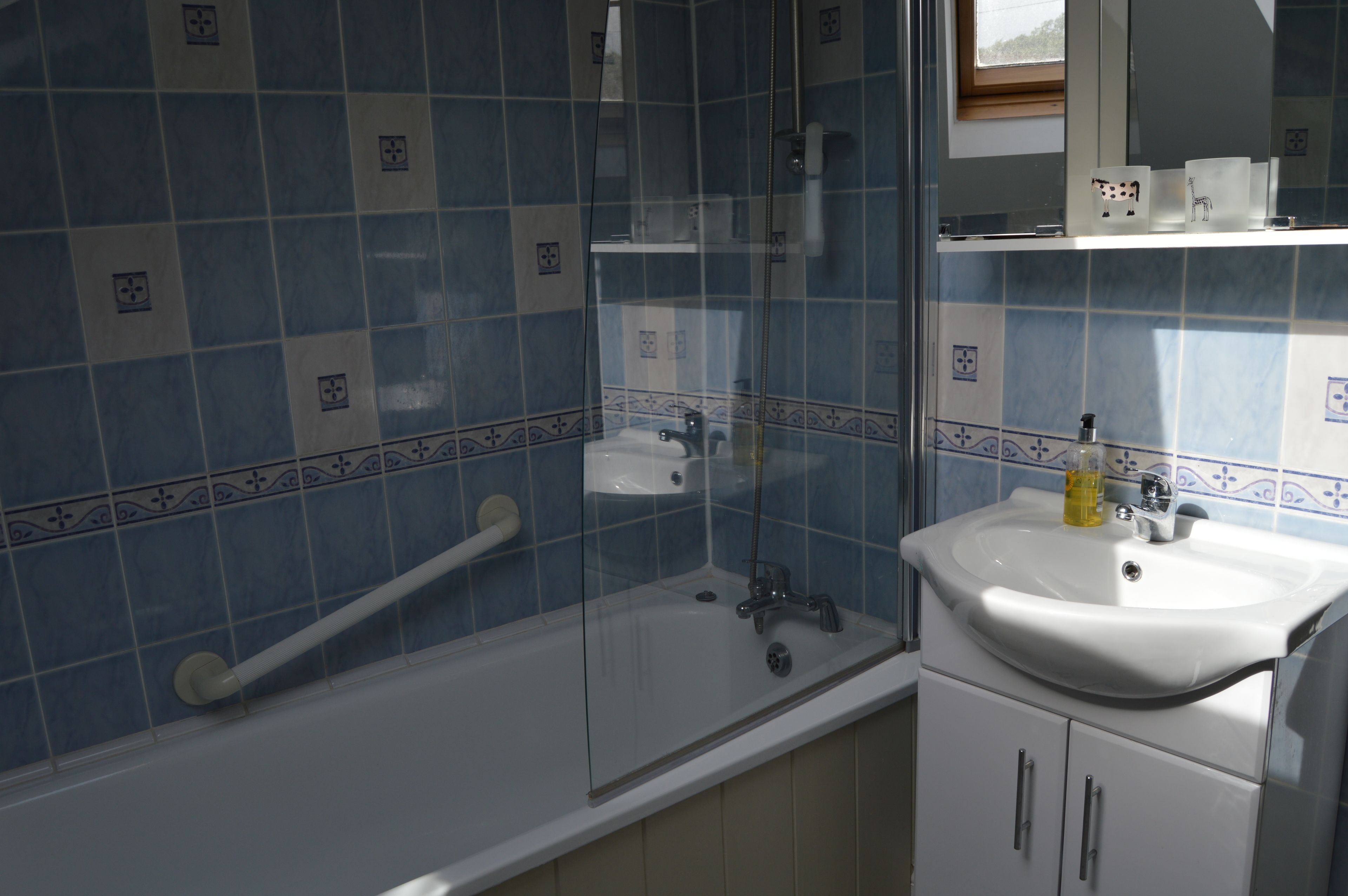 Een badkamer met blauwe tegels, een witte wastafel en een glazen douchecabine.