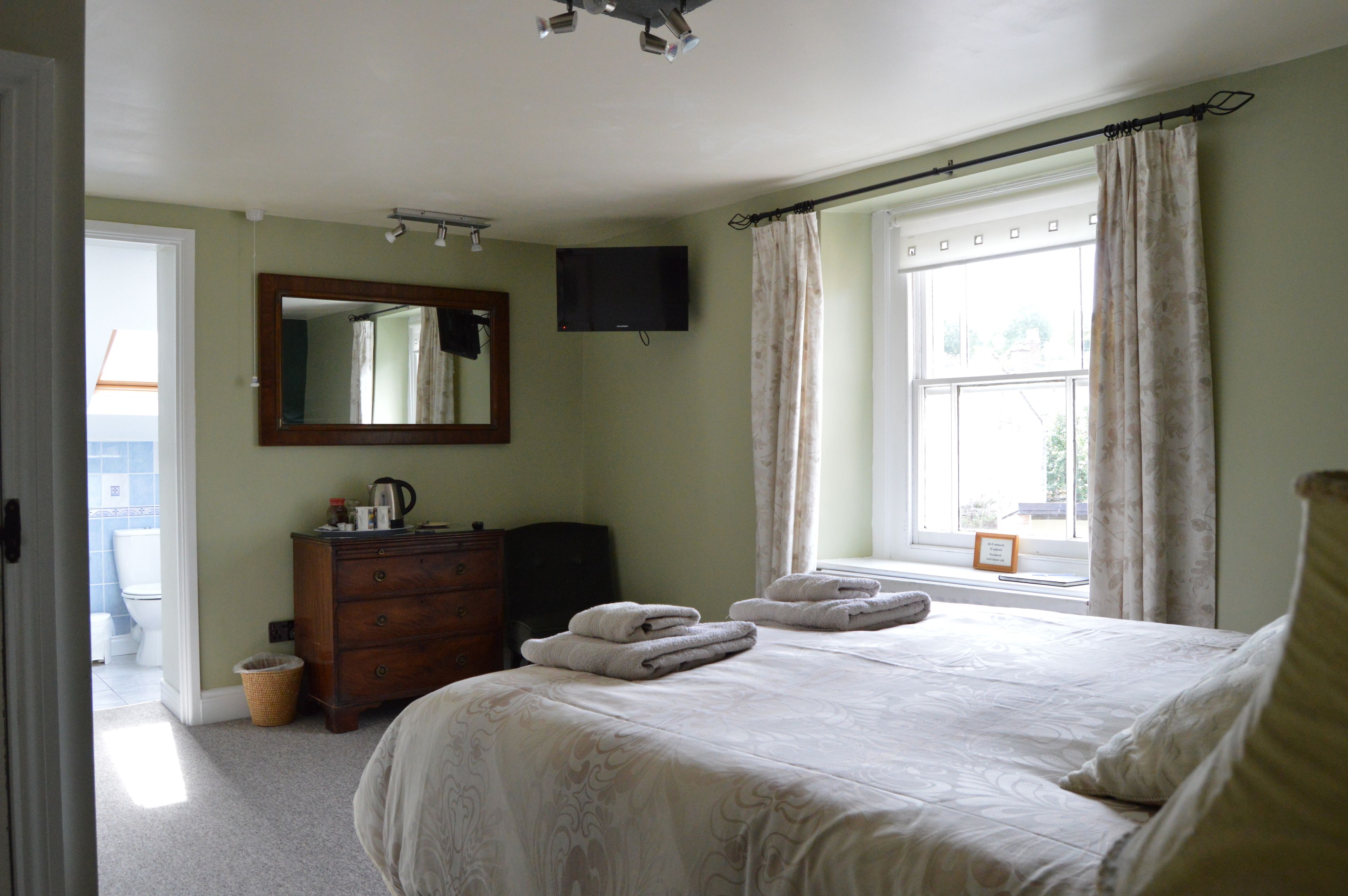 A bedroom with a bed, a dresser, a television, and a window with curtains.