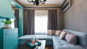 Un salon moderne avec un canapé bleu, une table basse sur laquelle se trouve un plateau, une plante en pot et une fenêtre avec des rideaux.
