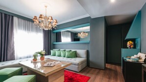 Un salon moderne avec une table basse en verre, des poufs verts, un tapis rouge, un canapé blanc avec des coussins verts et un mur d’accent bleu.