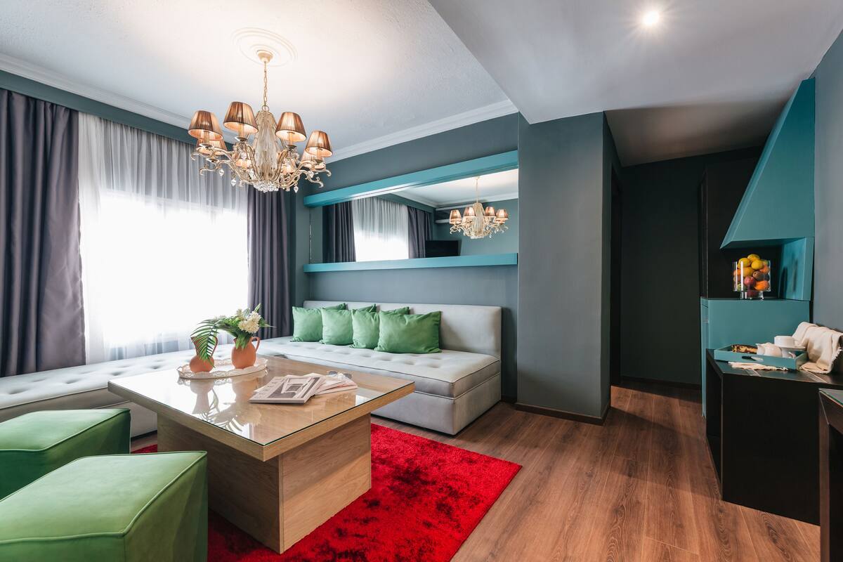 A modern living room with a glass coffee table, green ottomans, a red rug, a white sofa with green cushions, and a blue accent wall.