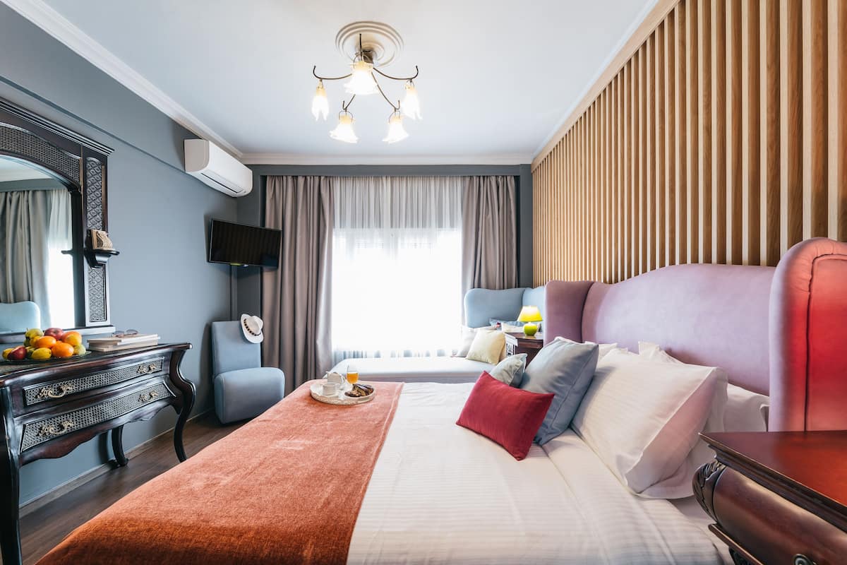 A hotel room with a large bed, a dresser, a television, and a window with curtains.