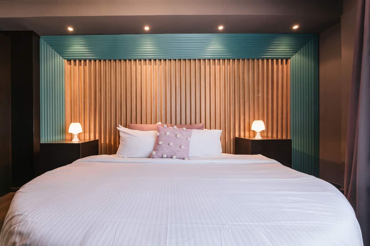 A neatly made bed with white linens, two bedside lamps, and a teal-colored headboard.