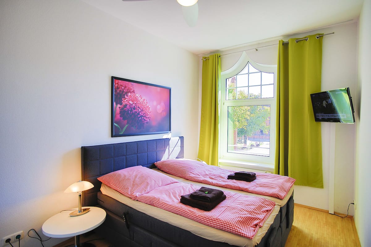 Un dormitorio con dos camas, una mesita de noche, un televisor y una ventana con cortinas.