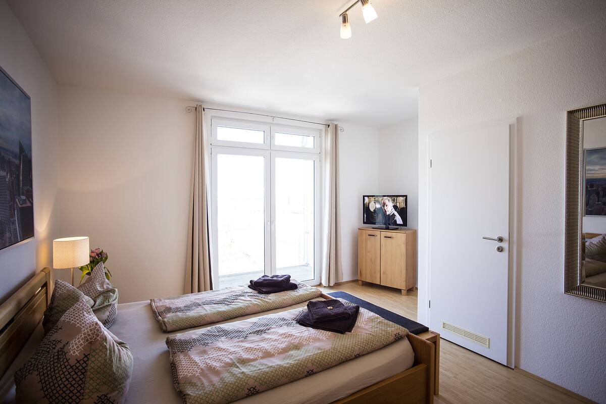 Habitación de hotel con dos camas, un televisor, un armario de madera y un ventanal grande.